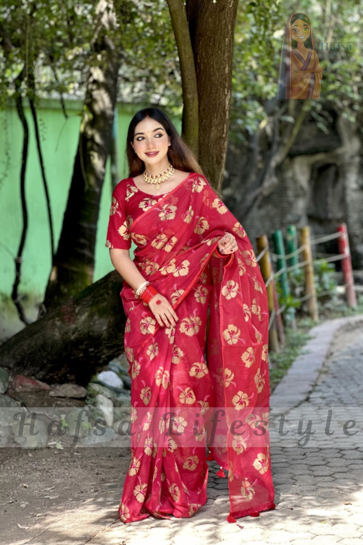 Woman in a red saree with gold patterns standing outdoors.