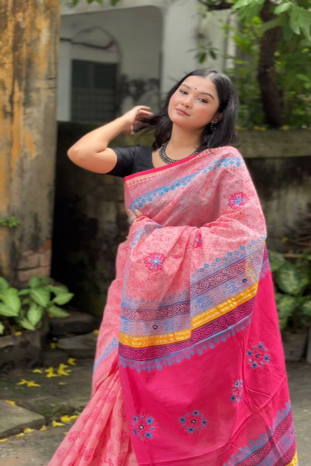 Woman wearing a pink saree with a colorful border outdoors.