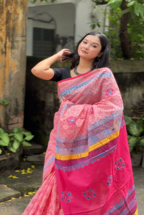 Woman wearing a pink saree with a colorful border outdoors.
